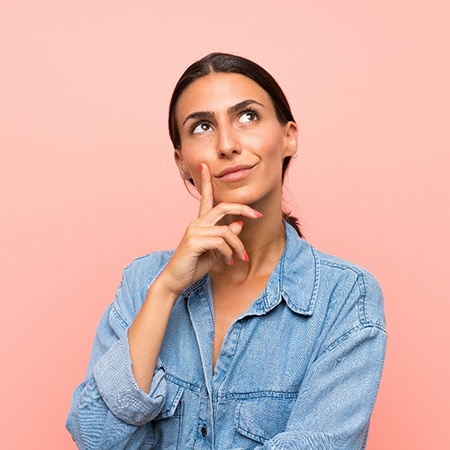 Woman with hand on chin thinking with pink background