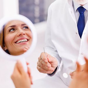 Dental patient holding mirror, smiling at her dentist