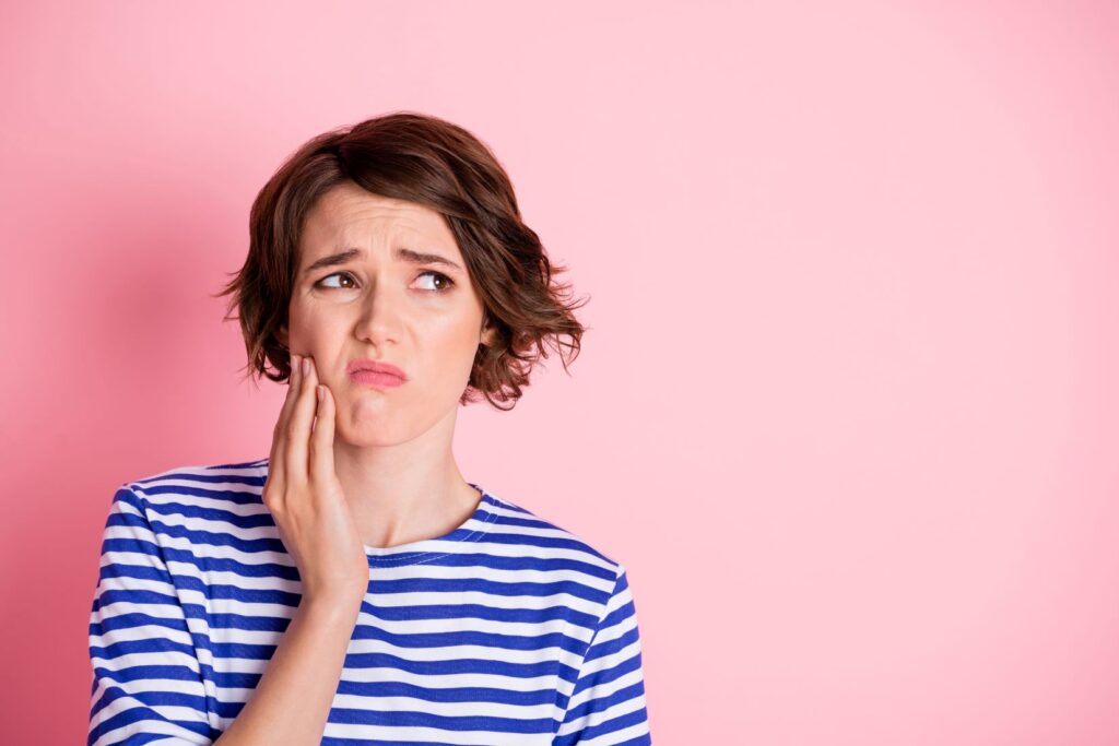 A young woman wincing in pain and holding her jaw.